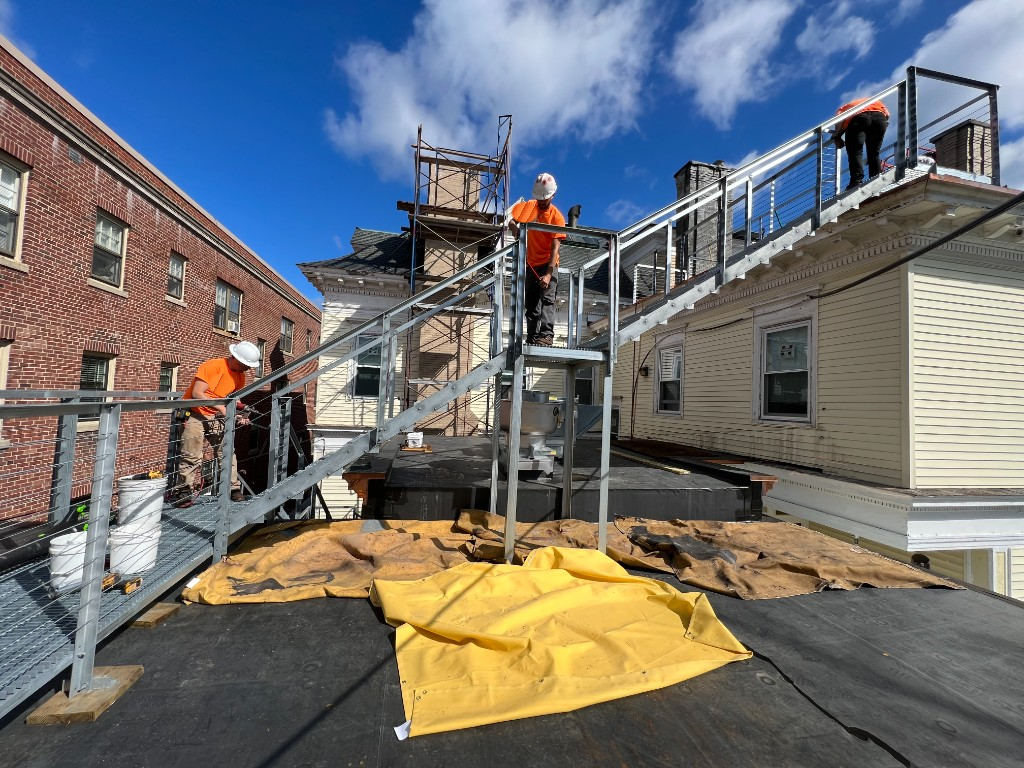 Ironworks Network crew installing galvanized steel rooftop access stair with open grating treads and cable railings, Greater Boston