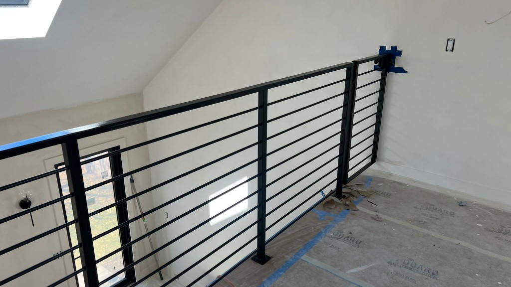 Black horizontal bar railing along an interior loft edge under a skylight