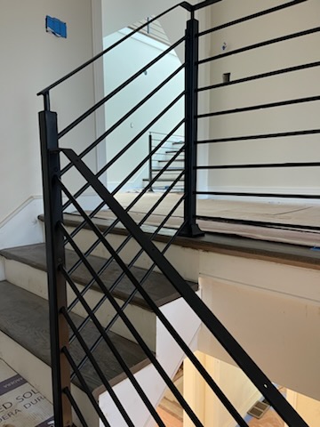 Close view of a black stair rail with horizontal bars and a cross panel