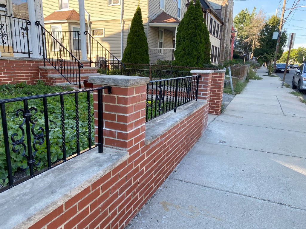 Ornamental black iron fence on brick wall with stone caps, residential Massachusetts frontage
